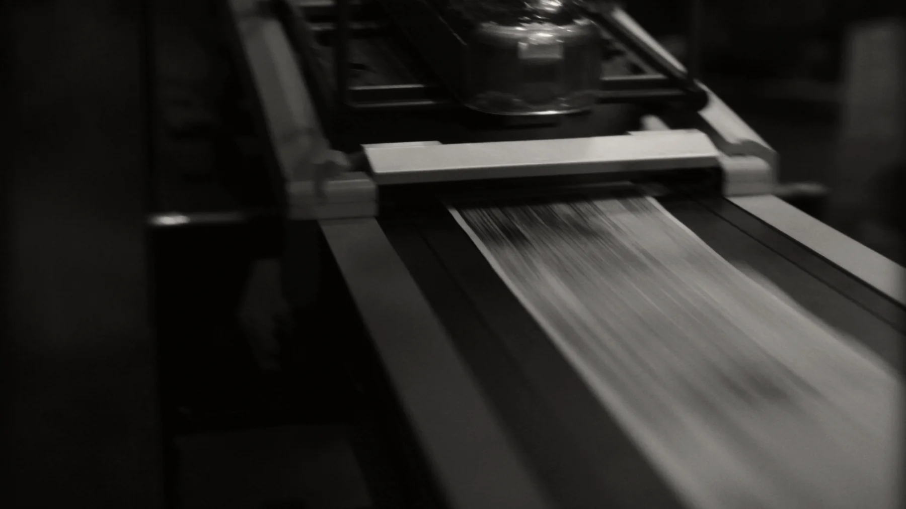 An inkjet addressing head over a moving stream of postcards on a vacuum belt, the cards blurred with speed and the head sharp.